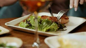 Female cuts a salmon steak on a plate with a fork and a knife, close-up. Dinner in a restaurant video