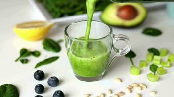 Woman is preparing a healthy detox drink in a blender - a  green smoothie with fresh fruits, green spinach and avocado. Healthy eating concept, ingredients for smoothies on the table, top view. video