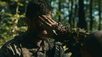 ein Hand Abstriche Schlamm auf das Gesicht von ein bärtig Soldat im das Wald video