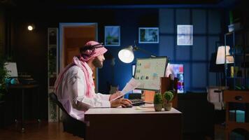 Muslim teleworker crosschecking analytics statistical data set with paperwork while remotely working in dimly lit apartment office. Hardworking Arab employee optimizing key performance indicators video