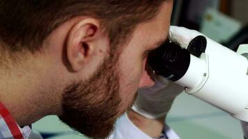 hombre mira dentro el oculares de microscopio a el laboratorio video