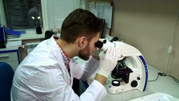 Man moves stage clipse on microscope at the laboratory video