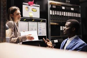 Team discussing bookkeeping report, working late at night at bureaucracy record in storage room. Diverse depository workers analyzing administrative documents, discovering accountancy files photo