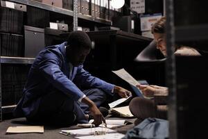 Diverse bookkeepers analyzing management research, working at accountancy report. Depository workers checking administrative documents, searching for bureaucracy record in storage room photo