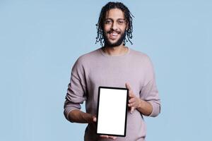 Smiling arab man showing digital tablet with white empty screen for application advertisement mock up. Happy person presenting portable gadget with blank touchscreen for product promotion photo