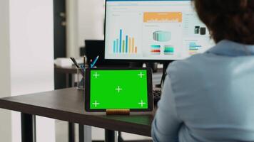 Company employee having tablet on desk with greenscreen display in startup agency office, using blank mockup template and isolated chromakey layout. Woman looking at digital web app on device. video