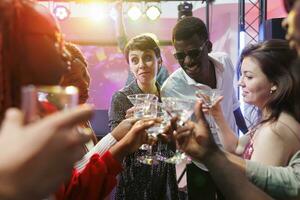 Cheerful young clubbers clinking glasses with beverages, saying toast and celebrating. Carefree smiling people crowd drinking alcohol while attending party gathering in nightclub photo