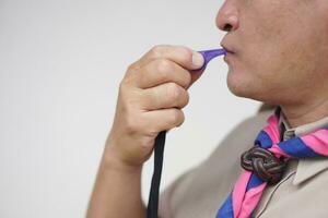 Close up man wears boy scout uniform is blowing the whistle. Concept, Scout blow whistle as meaningful sign for doing activity to assembly, start competition or playing games in scout lesson. photo