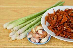 Fresh lemongrass, bowls of garlic and dried chillies on brown wooden floor. Concept, food ingredients, prepared for cooking. Herbal plants in Thai kitchen for various menus. photo