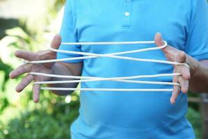 Closeup man hands is playing rope which called cats cradle game. Concept, game involving the creation of various style figures between the fingers. Traditonal playing. photo