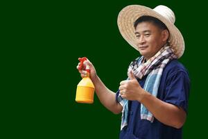 Asian man farmer wears hat, blue shirt, Thai loincloth scarf and holds spray bottle, thumbs up, isolated on green background. Concept, Agriculture occopation. photo