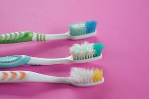 Three used, old toothbrushes on pink background. Concept, tool for brush teeth. Need to change new one from long time using toothbrush for efficiency of dental cleaning. photo