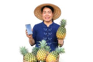 Asian fruit seller wear hat, blue shirt, holds pineapple fruit and smartphone , isolated on white background. Concept, Selling agriculture crops, using online device to promote sell photo