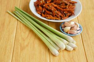 Fresh lemongrass, bowls of garlic and dried chillies on brown wooden floor. Concept, food ingredients, prepared for cooking. Herbal plants in Thai kitchen for various menus. photo