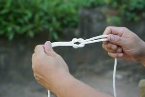 Close up man hands demonstrates how to tie knots on  white rope knot pattern. Concept, practice to tie different pattern of rope to apply in daily life such as tying things or doing  activities. photo