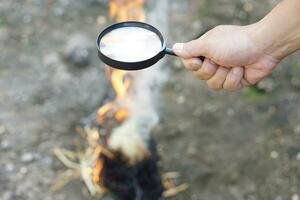 Close up hand held magnifying glass to make fire for burning dried hays.Concept, Science experiment about convex lens, hold magnifying glass between the sun and tinder. Handy survival skill photo