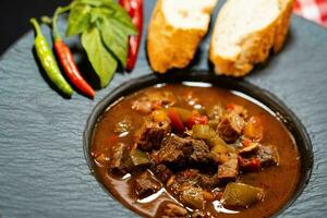 tradicional húngaro comida carne de vaca Estofado húngaro con un pan un picante pimientos foto