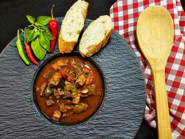 traditional Hungarian food beef goulash with bread an spicy peppers photo