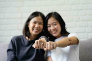 Young Asian couple is happy to show off their rings at home. Happy young Asian lesbian couple hugging each other in the living room at home. photo