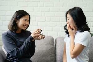Happy young Asian lesbian couple with wedding rings at home living room. LGBTQ lifestyle concepts. photo