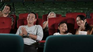 Various people in theater. Asian family, Kid, and parent audiences enjoy watching cinema and applauding together on movie stage, entertainment lifestyle with film art shows, happy and cheerful smiles. photo