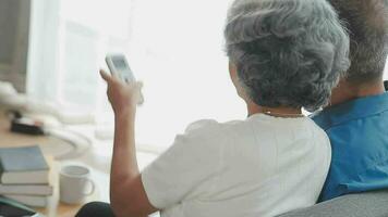 Happy senior couple using remote control to change channel. Seniors watch TV for entertainment while man using remote control. Wife and old man sitting on couch in living room with television show. video