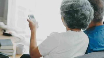 Happy senior couple using remote control to change channel. Seniors watch TV for entertainment while man using remote control. Wife and old man sitting on couch in living room with television show. video