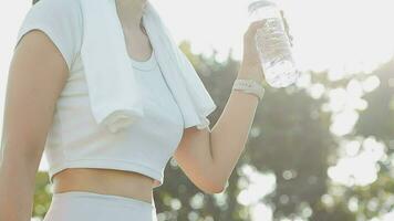 Jeune femme athlète prend une casser, en buvant eau, en dehors sur une courir sur une chaud journée. video