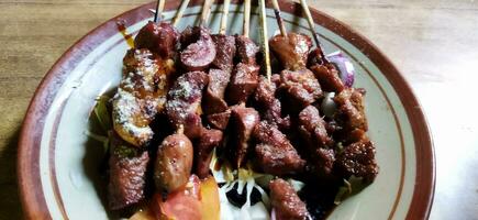 Satay or sate kambing, meat satay served with slice cabbage, red onion, chilli, tomatoes, with soy sauce on plate. Selective focus image photo