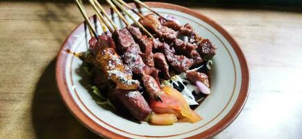 Satay or sate kambing, meat satay served with slice cabbage, red onion, chilli, tomatoes, with soy sauce on plate. Selective focus image photo