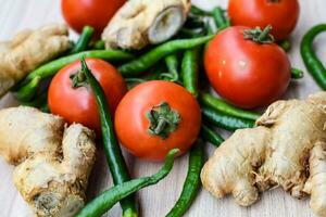 Fresh Ginger, Tomato and green chili pepper on plain wooden table, green essential vegetables for all essential foods, view of unpeeled vegetables with plain background photo