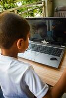 Little boy sitting at table using laptop for online class in Grade 1, Child studying on laptop from home for distance learning online education, School boy children lifestyle concept photo