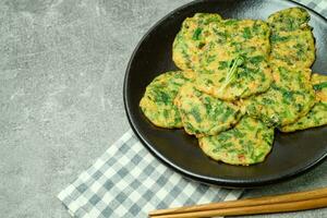 buchujeon, korean Chive Pancake, To prepare this dish, chive, julienned carrot, and green pepper are mixed with flour and pan-fried in a flat, round, pancake-like shape. photo