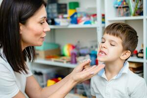 The speech therapist deals with the child and does an exercise to correct the speech apparatus using a straw or spaghetti photo