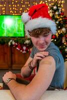 Portrait of a young male smiling after getting a vaccine - Man showing her arm with plaster during a Christmas party photo