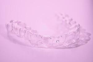 Invisible dental teeth brackets tooth aligners on pink background. Plastic braces dentistry retainers to straighten teeth. photo