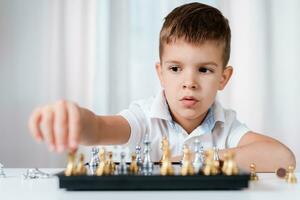 inteligente chico aprende a jugar ajedrez por él mismo en su habitación a hogar foto