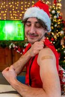 Portrait of a young male smiling after getting a vaccine - Man showing her arm with plaster during a Christmas party photo