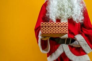 Papa Noel claus es demostración un regalo caja como un símbolo de amabilidad aislado en naranja antecedentes foto