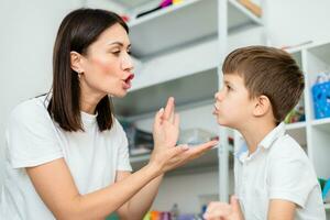 Cute woman speech therapist teaches child to pronounce words sounds and letters correctly in office photo