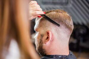 el Barbero cortes un barbado hombre con tijeras en el salón foto