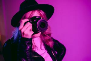 retrato de un hermosa niña fotógrafo en un sombrero quien toma imágenes en el estudio en un violeta antecedentes foto