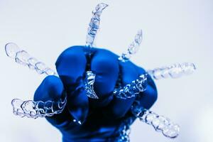 Invisible dental braces are held by a hand in a blue glove on a white background. Plastic braces dentistry retainers to straighten teeth. photo