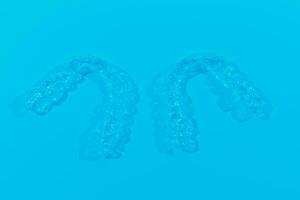 Invisible dental teeth brackets tooth aligners on blue background. Plastic braces dentistry retainers to straighten teeth. photo