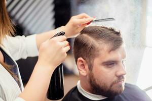 Hairdresser woman doing hairstyle to bearded man in barbershop photo