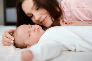 Young woman lovingly looks at her sleeping newborn daughter in the bedroom photo