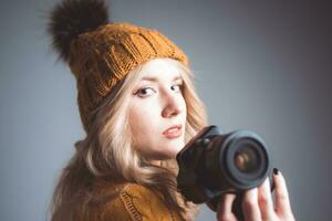 A beautiful woman photographer in a knitted hat is photographed with a camera in her hands in a photo studio