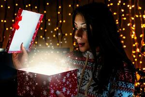cute young woman surprised opening christmas present from magic lights photo