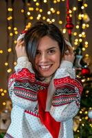 portrait of cute smiling young woman dressed in red hat and christmas sweatshirt posing in front of christmas lights photo