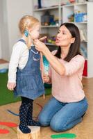 Woman speech therapist helps cute girl to learn correct pronunciation and literate speech photo